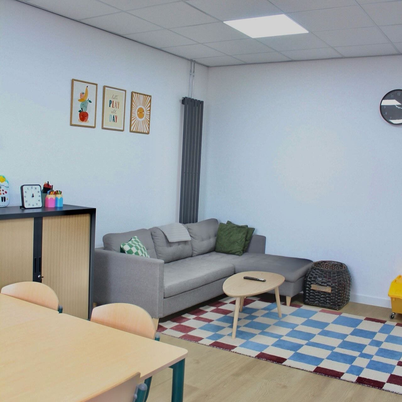 De woonkamer van Unique met een grijze bank, een geruit vloerkleed en een grote tafel.